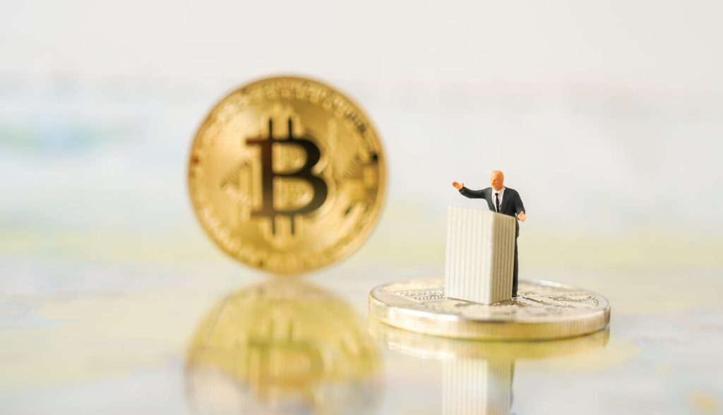 miniatura de homem sob pulpito e moeda gigante de bitcoin ao lado