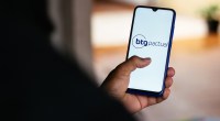 Uma pessoa de costa mexe no celular com logotipo do banco BTG Pactual