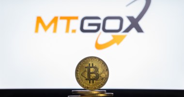 Moeda de Bitcoin à frente de logo da Mt. Gox