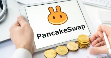 Tela de tablet mostra logotipo da PancakeSwap e moedas douradas aolado