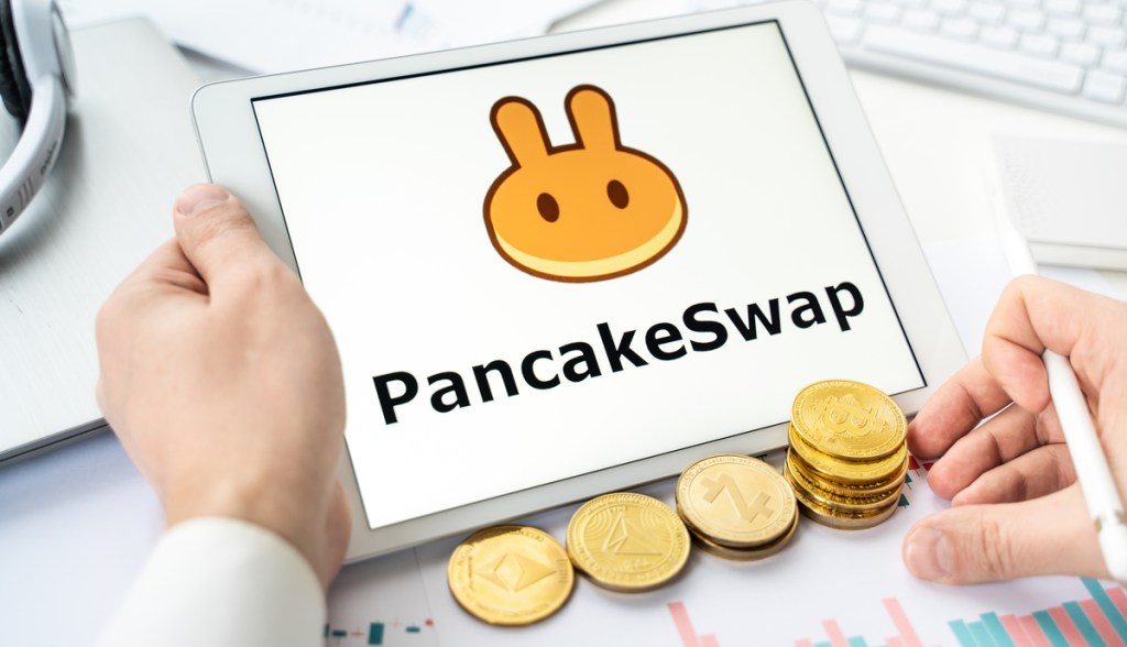 Tela de tablet mostra logotipo da PancakeSwap e moedas douradas aolado