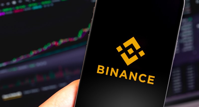 Celular com logo da Binance e gráfico no fundo