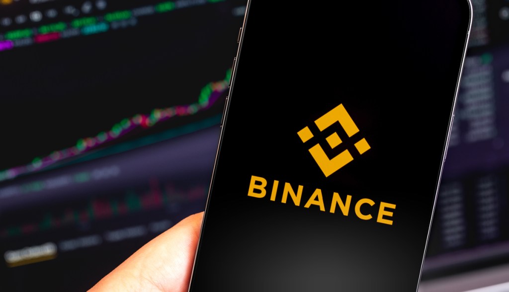 Celular com logo da Binance e gráfico no fundo