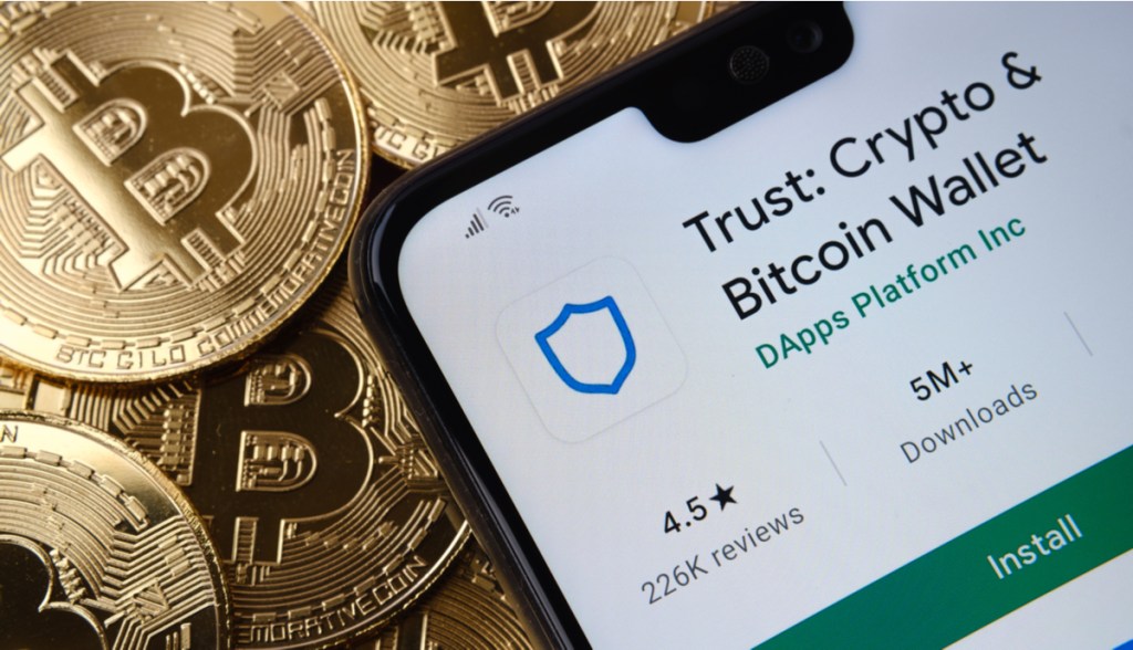 celular mostra logo da Trus Wallet ao lado de moedas de Bitcoin
