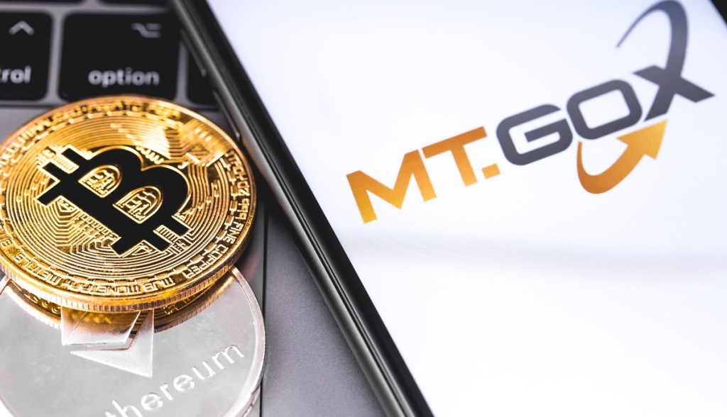Moeda de bitcoin ao lado de smartphone com logotipo da corretora Mt.Gox