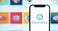 Celular à frente de grande tela de computador mostra logo da Opensea