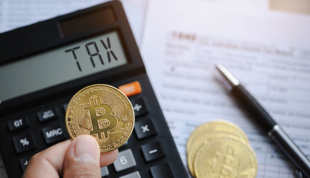 Uma pessoa segura uma moeda de bitcoin na frente de uma calculadora com o termo taxa