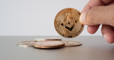 Um pessoa segura moeda Binance Coin BNB com a ponta dos dedos