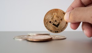 Um pessoa segura moeda Binance Coin BNB com a ponta dos dedos