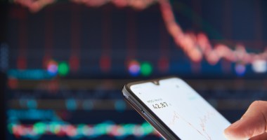 Celular com gráficos de ações e criptomoedas em queda no fundo