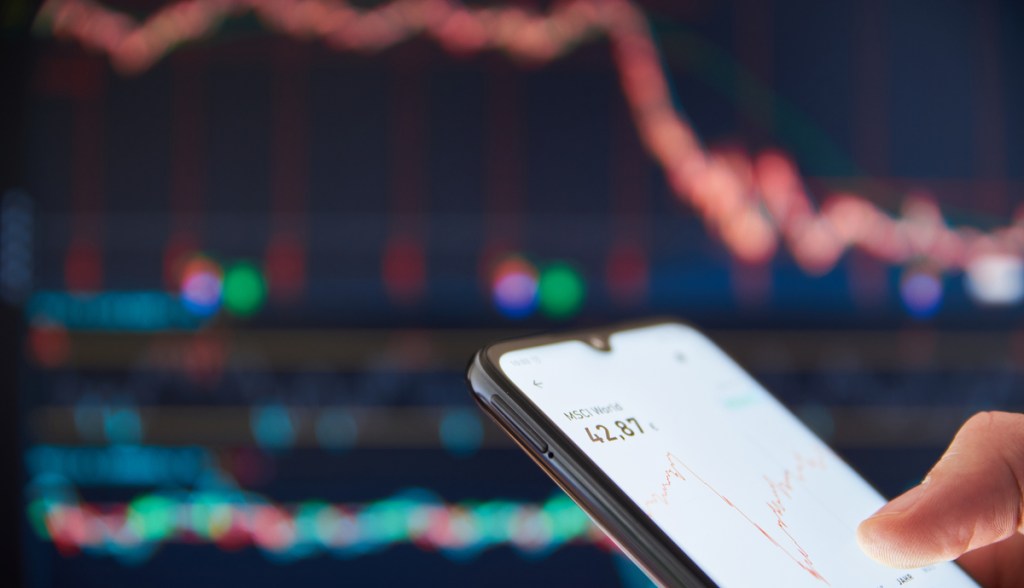 Celular com gráficos de ações e criptomoedas em queda no fundo