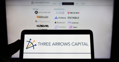 Celular com imagem da Three Arrows Capital na frente dela com logos do bitcoin e criptomoedas