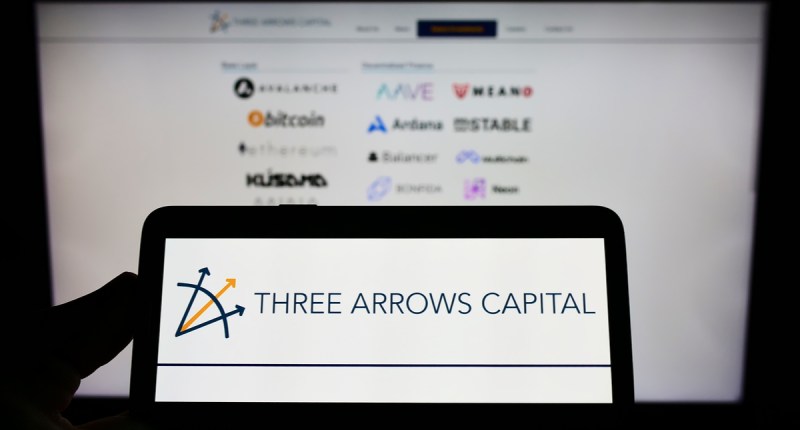 Celular com imagem da Three Arrows Capital na frente dela com logos do bitcoin e criptomoedas