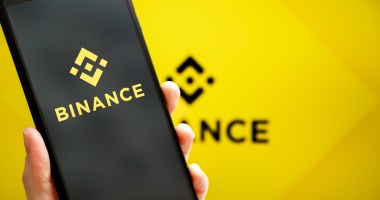 Celular com logo da Binance na frente de um fundo amarelo com logo da Binance.jpg