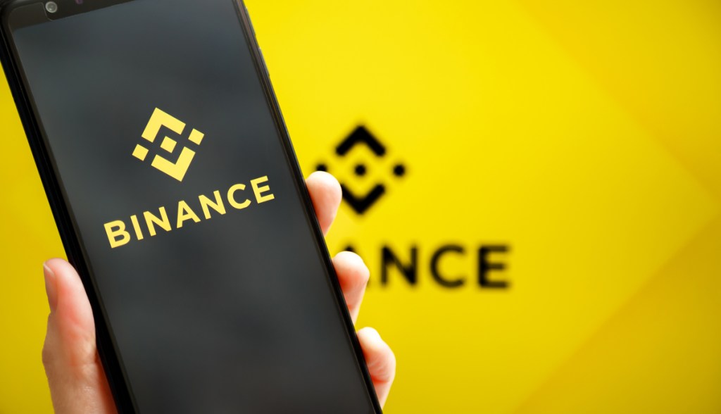 Celular com logo da Binance na frente de um fundo amarelo com logo da Binance.jpg
