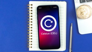 Celular com o logo da plataforma Celsius sobre um caderno e próximo a uma caneta e um notebook com moedas de Bitcoin em cima