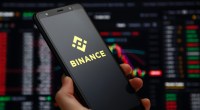 mão segurando celular com logo da binance e gráficos ao fundo