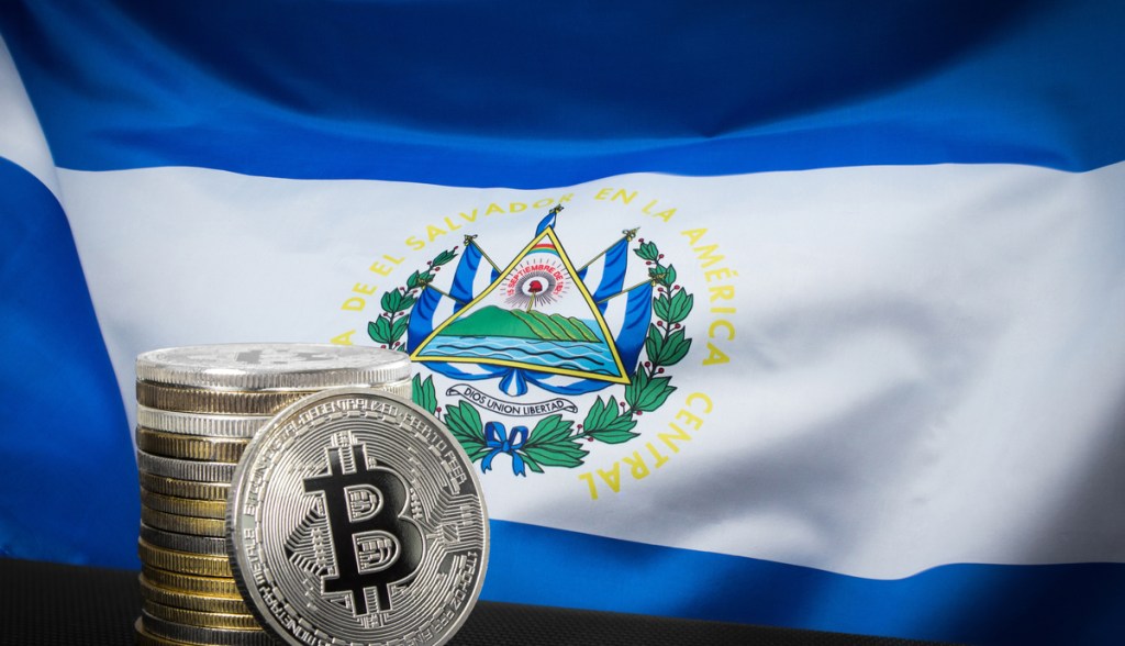 Bandeira de El Salvador ao fundo, e moedas de Bitcoin