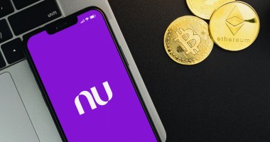 Foto com um celular aberto no aplicativo Nubank, e criptomoedas ao redor.