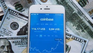 Celular com foco no logo da Coinbase e cédulas de dólar ao redor