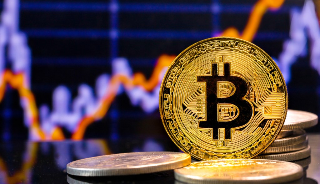 Moedas douradas de Bitcoin (BTC) e um gráfico de preço ao fundo