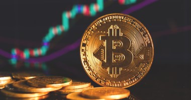 Moedas douradas de Bitcoin (BTC) em frente a um gráfico de preço de alta