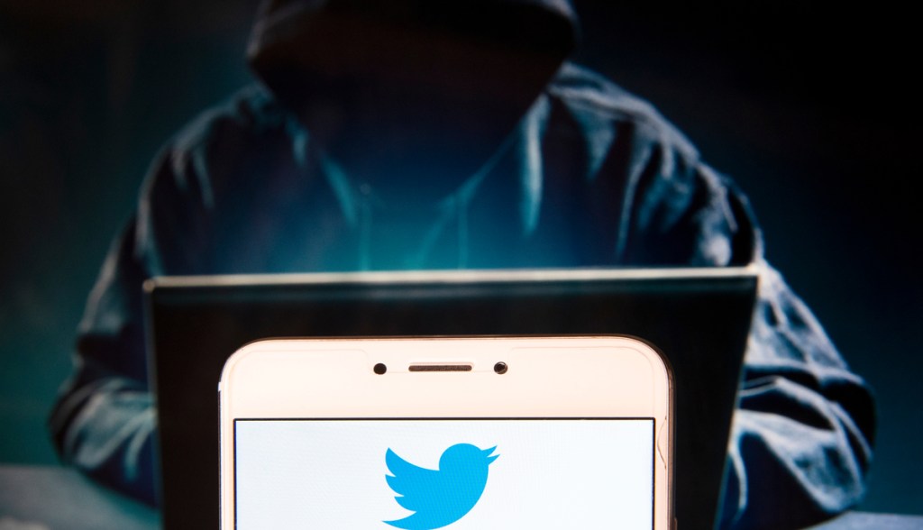 Pessoa encapuzada em um notebook- à frente o logo do Twitter logo do Twitter