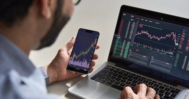 homem operando trading em celular e notebook