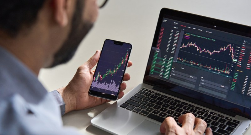 homem operando trading em celular e notebook