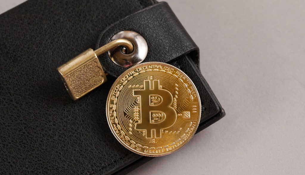 moeda de bitcoin em cima de uam carteira de bolso fechada com um cadeado