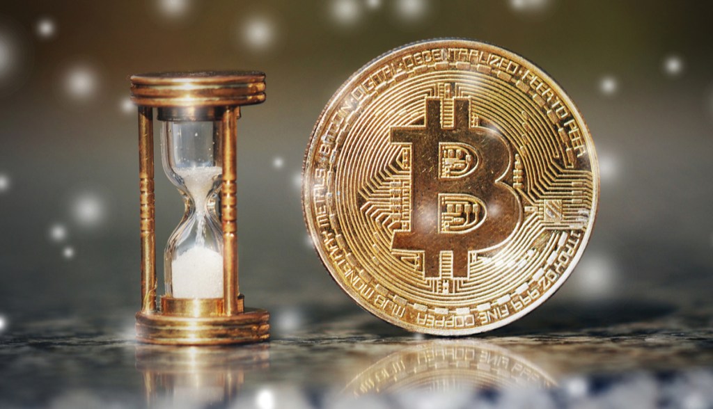 Ampulheta com tempo acabando ao lado de uma moeda de bitcoin