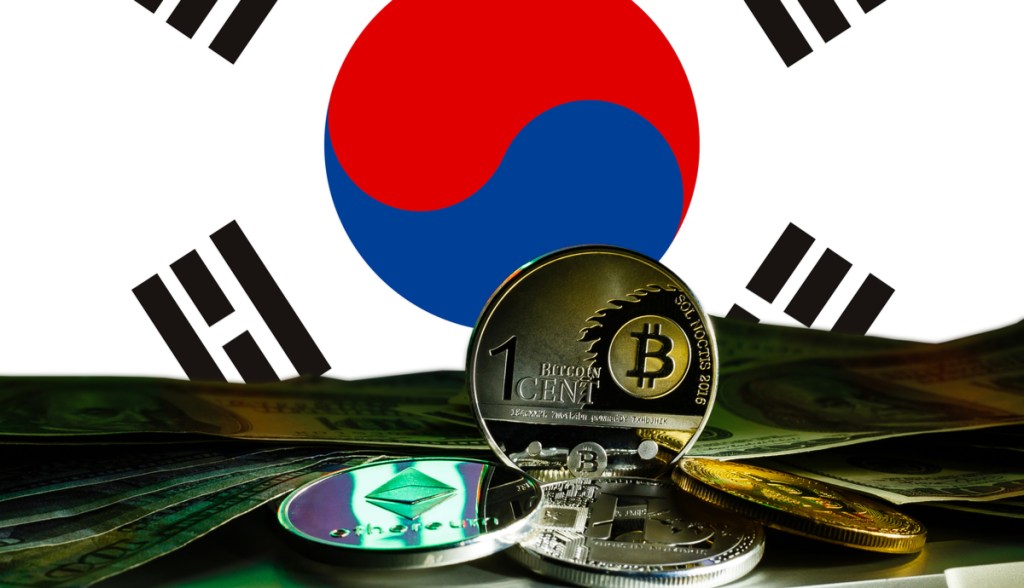 Criptomoedas sobre uma mesa e uma bandeira da Coreia do Sul ao fundo