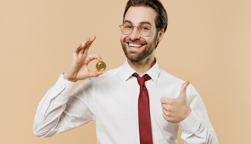 Homem de gravata segura contente uma moeda de bitcoin