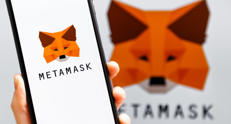 Mão segurando celular com o logo da carteira de criptomoedas MetaMask