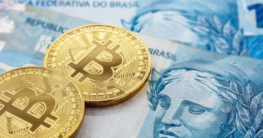 Moedas douradas de Bitcoin em cima de notas e cédulas de cem reais real