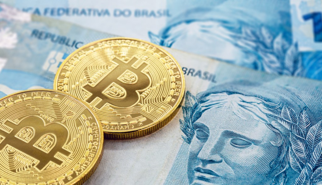 Moedas douradas de Bitcoin em cima de notas e cédulas de cem reais real