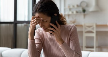 Mulher sentada em um sofá demonstra desespero ao ouvir mensagem no celular