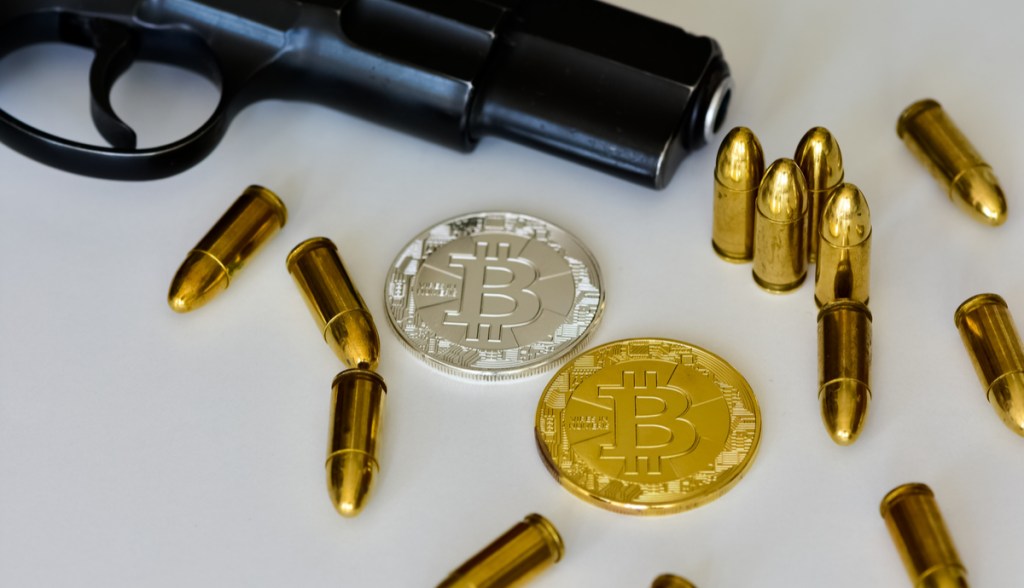 Uma pistola, munições e moeda de bitcoin sobre uma mesa