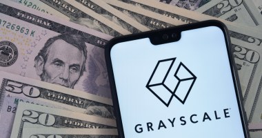 celular exibe logo da grayscale com notas de dólar ao fundo