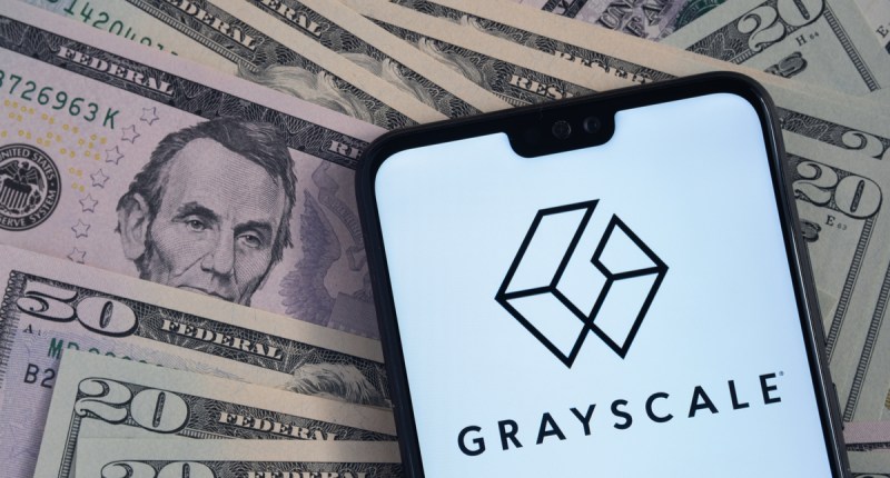 celular exibe logo da grayscale com notas de dólar ao fundo