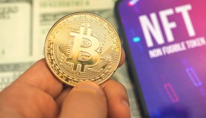 Dedos seguram moeda de bitcoin ao lado de tela que mostra sigla NFT