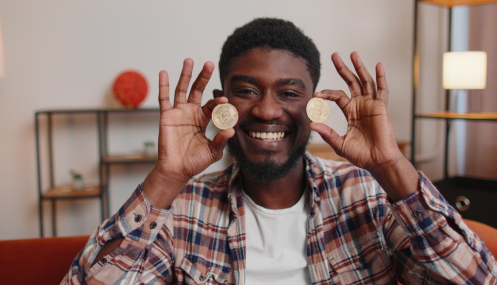 Homem preto sorrindo segura em ambas as mãos moedas de bitcoin