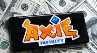 Smartphone sobre dólares mostra logo Axie Infinity