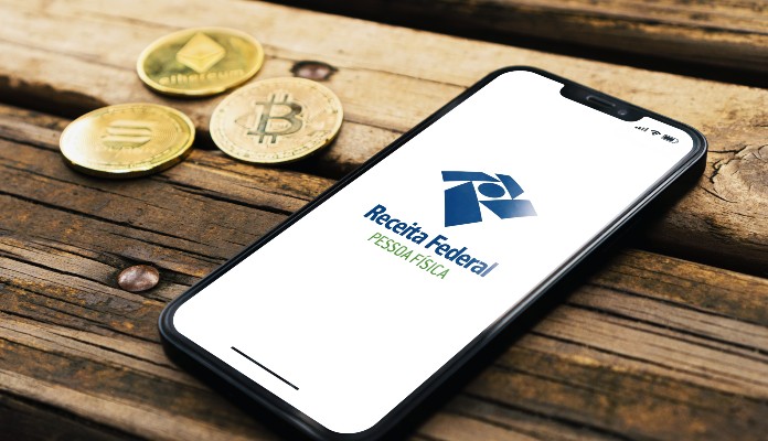 Celular com logo da Receita Federal e Bitcoin e criptomoedas do lado