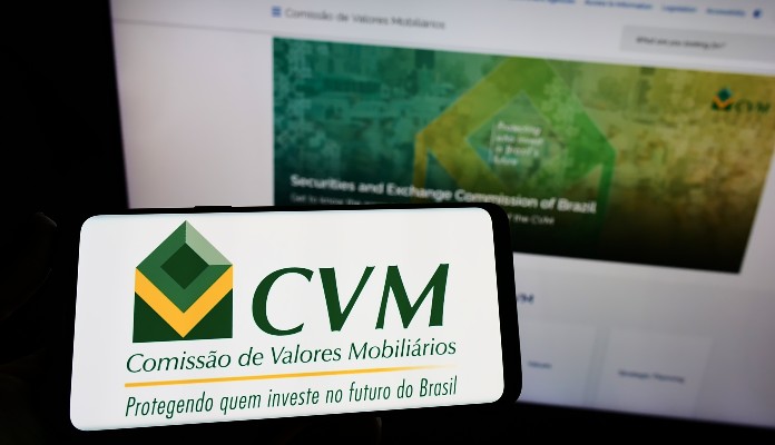 Celular com o logo da CVM e notebook aberto no site da Comissãod e Valores Mobiliários