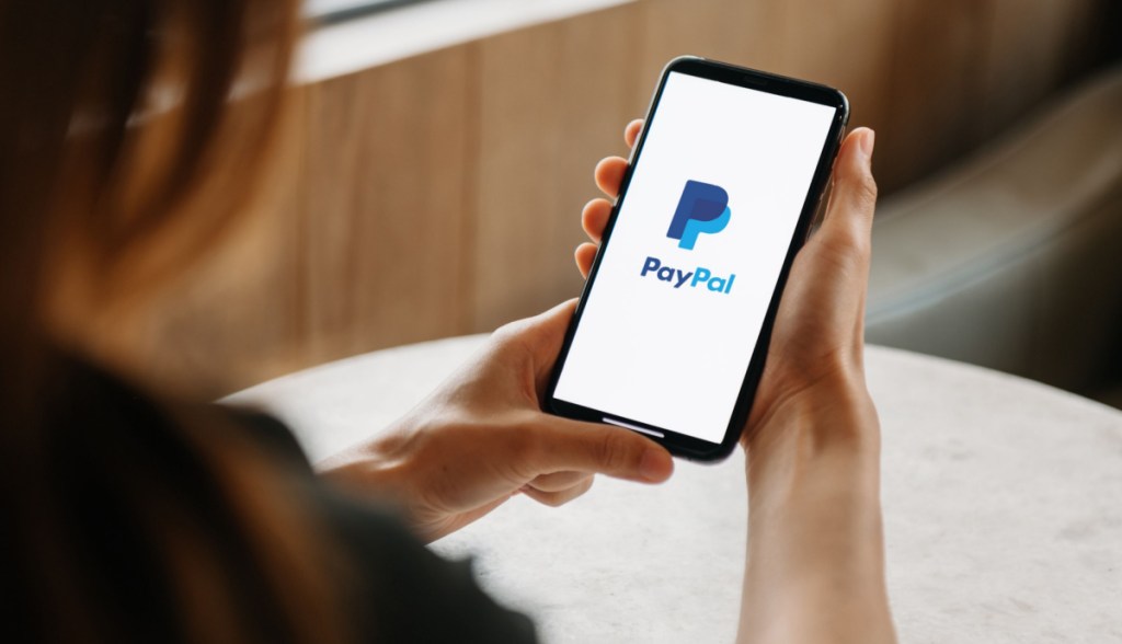 Mulher olhando celular com logotipo do paypal
