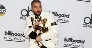 Drake, cantor e rapper, de terno branco segurando prêmios