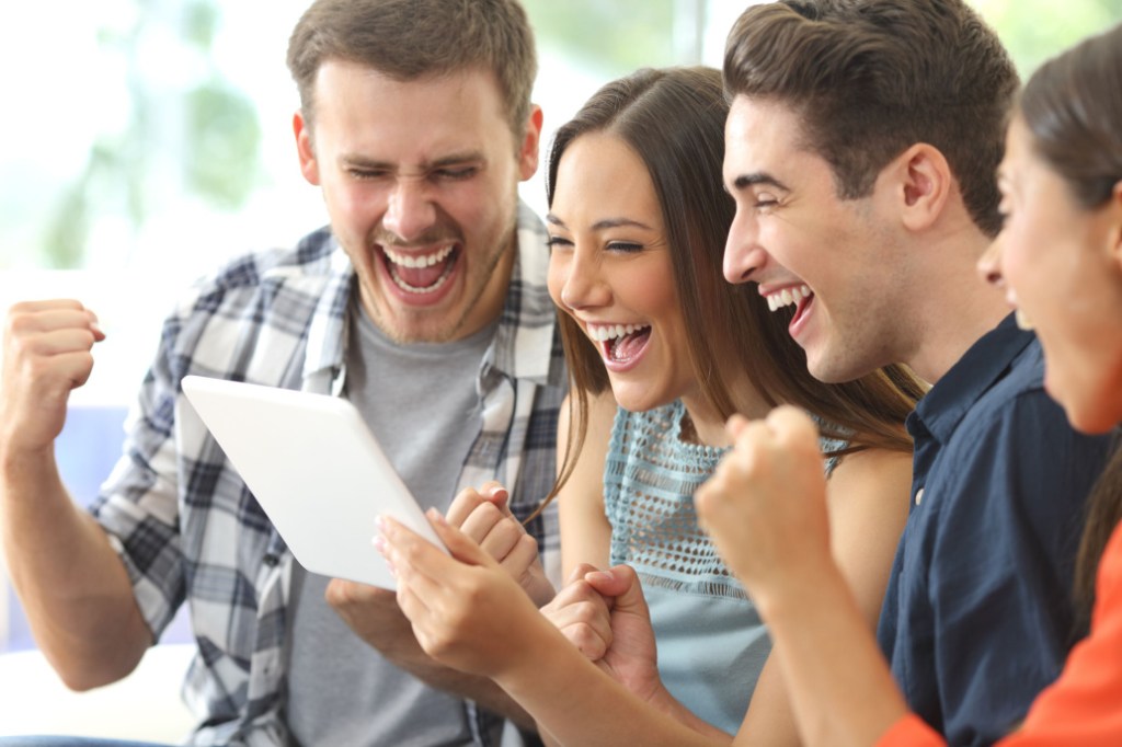quatro jovens homens e mulheres miram tablet e comemoram