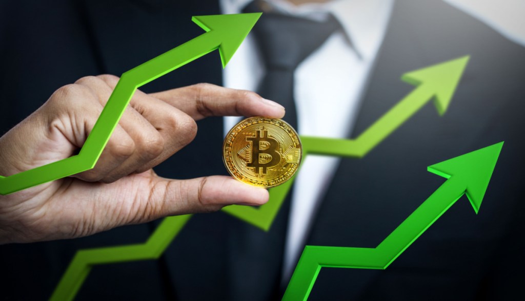 Homem segura moeda de bitcoin em meio a gráfico de alta