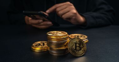 Um monte de moedas de bitcoin em mesa em que homem mexe no celular